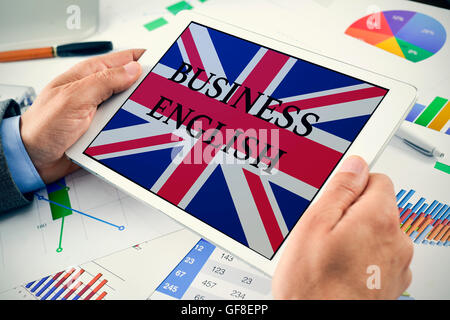 closeup of a young caucasian businessman at his office desk full of charts showing a tablet computer with the text business Engl Stock Photo