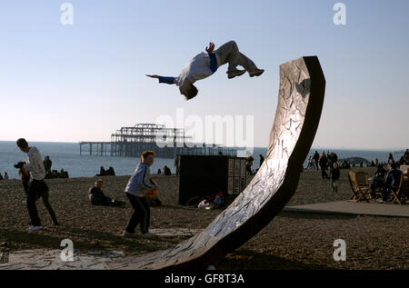 A youngster performs a spectacular back flip on one of the large sculptures on Brighton beach today as crowds enjoy the winter sunshine Stock Photo