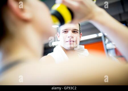 PROPERTY RELEASED. MODEL RELEASED. Man looking at woman while drinking water in gym. Stock Photo