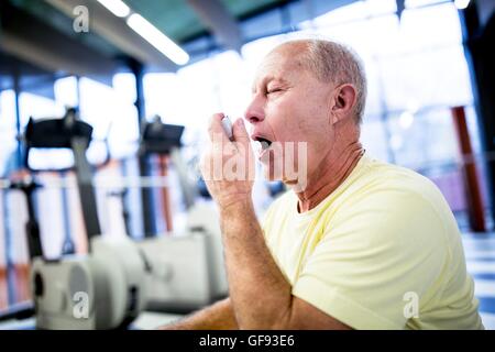 PROPERTY RELEASED. MODEL RELEASED. Senior man using asthma inhaler in gym. Stock Photo