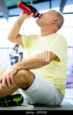 PROPERTY RELEASED. MODEL RELEASED. Senior man sitting and drinking water from water bottle in gym. Stock Photo