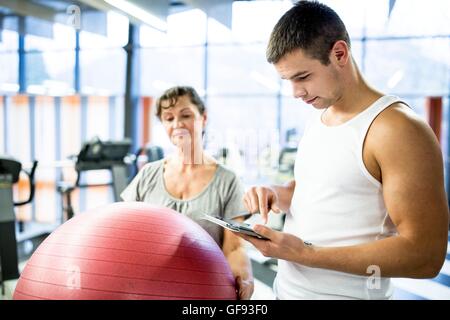 PROPERTY RELEASED. MODEL RELEASED. Young man using tablet and woman holding fitness ball in background. Stock Photo