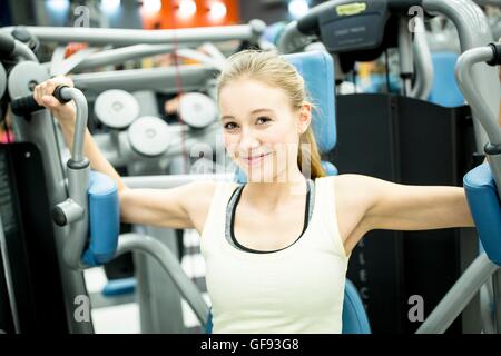 PROPERTY RELEASED. MODEL RELEASED. Portrait of young woman using butterfly machine in gym. Stock Photo