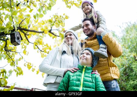 MODEL RELEASED. Family together in park smiling and looking away, birdhouse in background. Stock Photo
