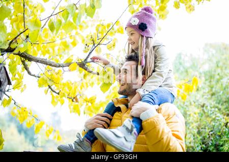 MODEL RELEASED. Father carrying daughter on shoulders and looking at branch in autumn. Stock Photo