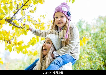 MODEL RELEASED. Mother carrying daughter on shoulders and looking at branch in autumn. Stock Photo