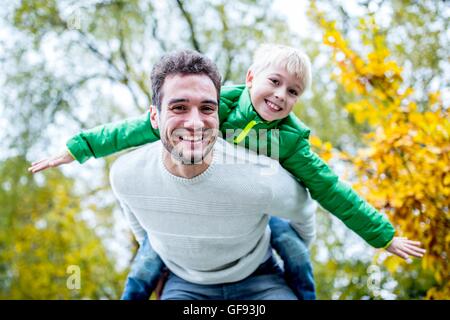 MODEL RELEASED. Father carrying son piggyback in autumn, smiling, portrait. Stock Photo