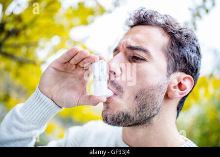 MODEL RELEASED. Young man using asthma inhaler, close-up. Stock Photo