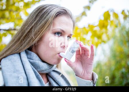 MODEL RELEASED. Young woman using asthma inhaler, close-up. Stock Photo