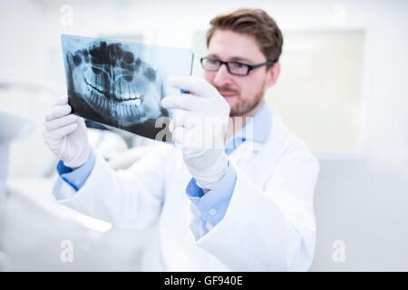 MODEL RELEASED. Dentist looking at x-ray image with dental assistance in background. Stock Photo