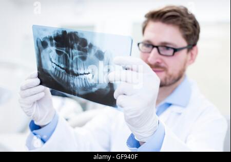 MODEL RELEASED. Dentist looking at x-ray image with dental assistance in background. Stock Photo