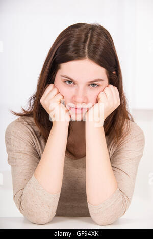 MODEL RELEASED. Sad young woman with hands on chin, studio shot. Stock Photo