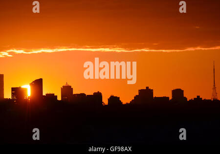 Glowing orange sun setting behind city buildings in silhouette (North Sydney, Australia) Stock Photo