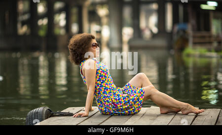 Asian young woman posing sitting on the pier near river. Stock Photo