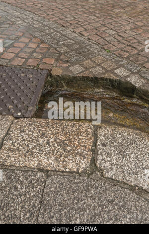 Street drainage / gutter in Truro, Cornwall. Visual metaphor for 'money down the drain' and water waste / wasting water. Stock Photo