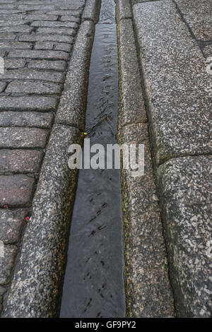 Street drainage / gutter in Truro, Cornwall. Visual metaphor for 'money down the drain' and water waste / wasting water. Stock Photo