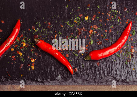 Chillies on a slate with a mixture of chilli flakes and herbs scattered around. Stock Photo