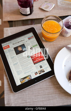 View of an Apple iPad device displaying the New York Times newspaper's nytimes.com homepage on a table with breakfast served. Stock Photo