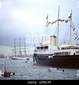 AJAXNETPHOTO. - JULY, 1991. - MILFORD HAVEN, WALES. - DRESSED OVERALL - HMRY BRITANNIA AT MILFORD HAVEN FOR THE TALL SHIPS REGATTA. THE POLISH SHIP DAR MLODZIEZY IS IN THE BACKGROUND. PHOTO:JONATHAN EASTLAND/AJAX REF:920348 Stock Photo