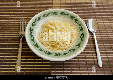 spaghetti in bowl with fork and spoon on a bamboo mat Stock Photo