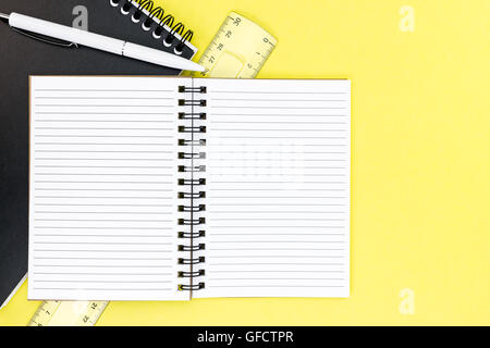 notepad, ruler, ballpoint pen and opened ruled notebook on yellow writing desk background Stock Photo