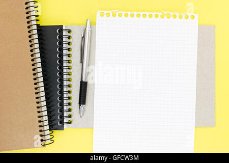 empty squared sheet of paper from notepad and ballpoint pen on yellow writing desk Stock Photo