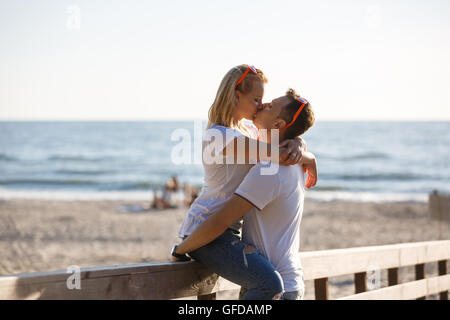 Young couple are kissing by the wooden fence on the beach, summer time Stock Photo