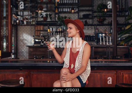 Portrait of stylish young woman having a drink at cafe. Caucasian female sitting at coffee shop counter holding a glass of drink Stock Photo
