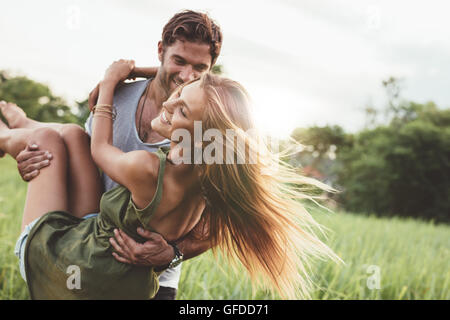 Shot of young woman being carried by her boyfriend in grass field. Couple having fun on their summer holiday. Stock Photo