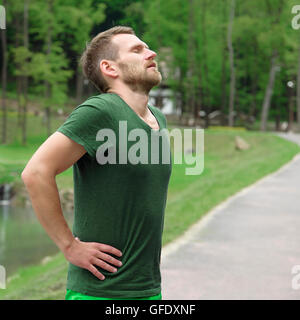 Runner resting tired and exhausted after running. Jogging man taking a break during training outdoors in on mountain road. Stock Photo