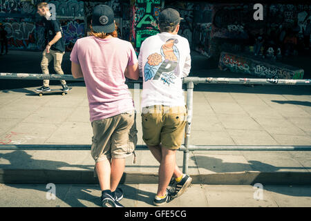 Two young men watch skateboarders doing tricks under the Royal Festival Hall in the Southbank Centre, London, UK Stock Photo