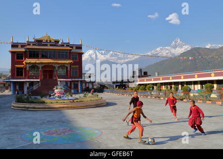 Monks playing football outside a Tibetan temple near Pokhara, Nepal, Himalaya mountains with Machapuchare Peak in background Stock Photo