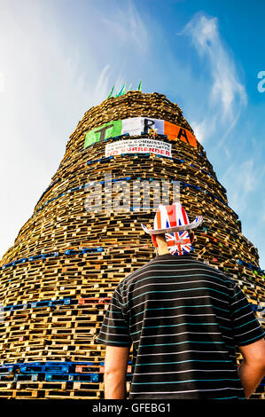 Belfast, Northern Ireland, 11th July 2013 - A man wearing a union flag hat looks up at the Shankill Road bonfire, which carries Stock Photo