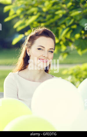 Young happy woman with bunch of balloons in summer park. Beautiful girl in dress at summer time Stock Photo