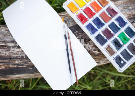 Mock up with blank paper notebook and watercolor set with brushes lying on the old wood. Top view image Stock Photo