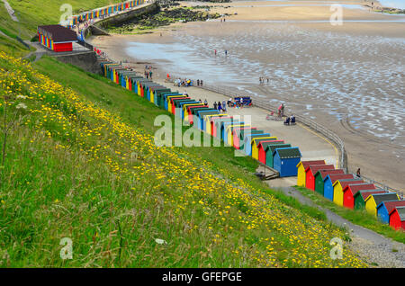 Multi-coloured beach huts at Whitby Beach, Whitby, Yorkshire, England, UK. Sandsend in the distance Stock Photo