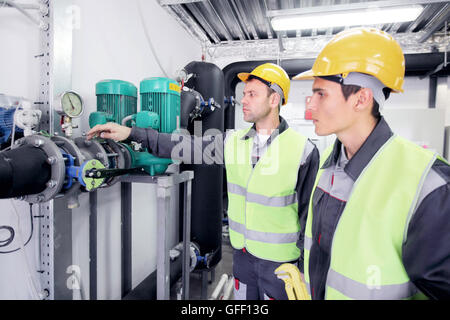 Two workers in hardhats at plant checking parameters of pressure Stock Photo