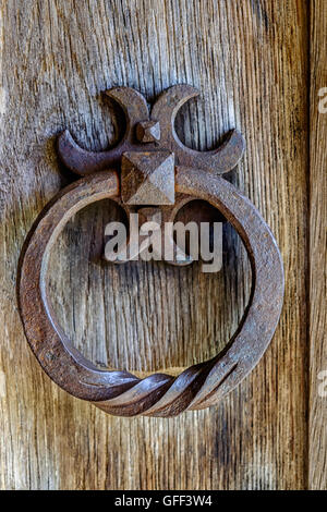 Ornate ancient rusty iron door knocker on section of wooden door Stock Photo