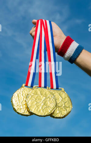 Hand of American athlete holding gold medals hanging from USA colors red, white, and blue ribbon against a blue sky background Stock Photo