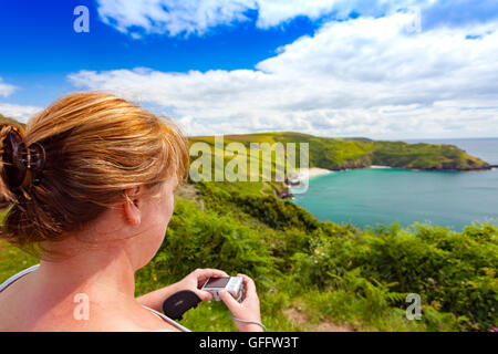 Woman taking a photograph of Lantic Bay, Cornwall, UK with the camera in shot on a summers day Stock Photo