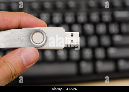 Hand hold blank USB thumb drive with keyboard in the background Stock Photo