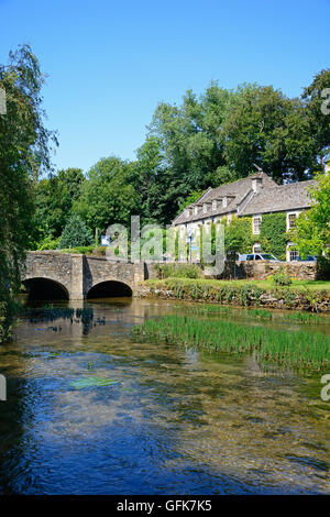View along the River Coln towards the stone bridge with The Swan Hotel to the rear, Bibury, Cotswolds, Gloucestershire, England, Stock Photo