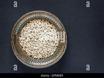 Antique metal bowl of raw hulled sunflower seeds on a dark textured background Stock Photo