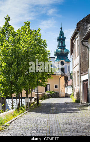 Small street on a hill in the medieval city Banska Stiavnica, Slovakia. Old houses and a tower of a church. Blue summer sky with Stock Photo