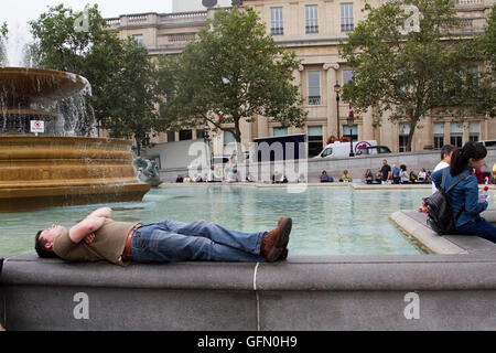 London,UK. 1st August 2016. A man snoozes on the edge of Trafalgar Square fountain on a warm overcast day in London Credit:  amer ghazzal/Alamy Live News Stock Photo