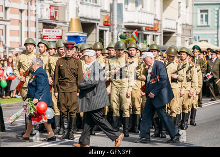 The Elderly Honored WW2 Veterans Pass Near The Line-Up Of Armed Soldiers In Soviet WWII Uniform, Officer In Front. Re-Enactors P Stock Photo