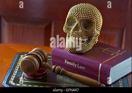 Smiling gold themed human like skull on Family Law book with judges gavel on inlaid desk ‘The last laugh’ Stock Photo