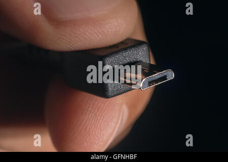 Hand holding black micro USB cable. Man's hand holds a USB micro Connector. Closeup man hand holding micro USB cable. Stock Photo