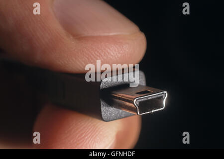 Hand holding black mini USB cable. Man's hand holds a USB mini Connector. Closeup man hand holding mini USB cable. Stock Photo