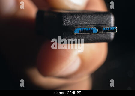 Hand holding black micro USB 3.0 cable. Man's hand holds a USB Connector. Closeup man hand holding USB cable. Stock Photo